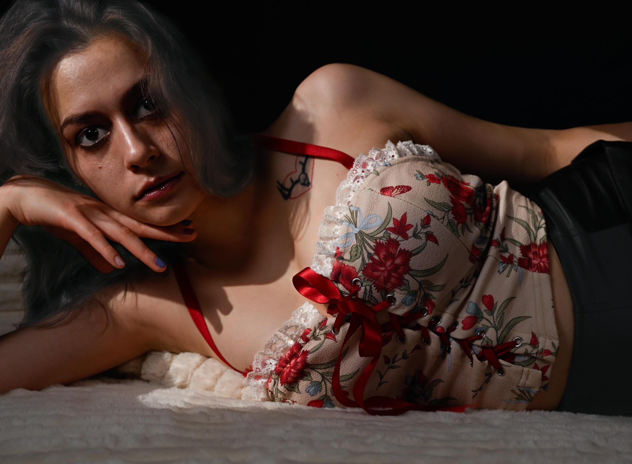 Reclining studio portrait of a woman in a floral corset with red ribbons