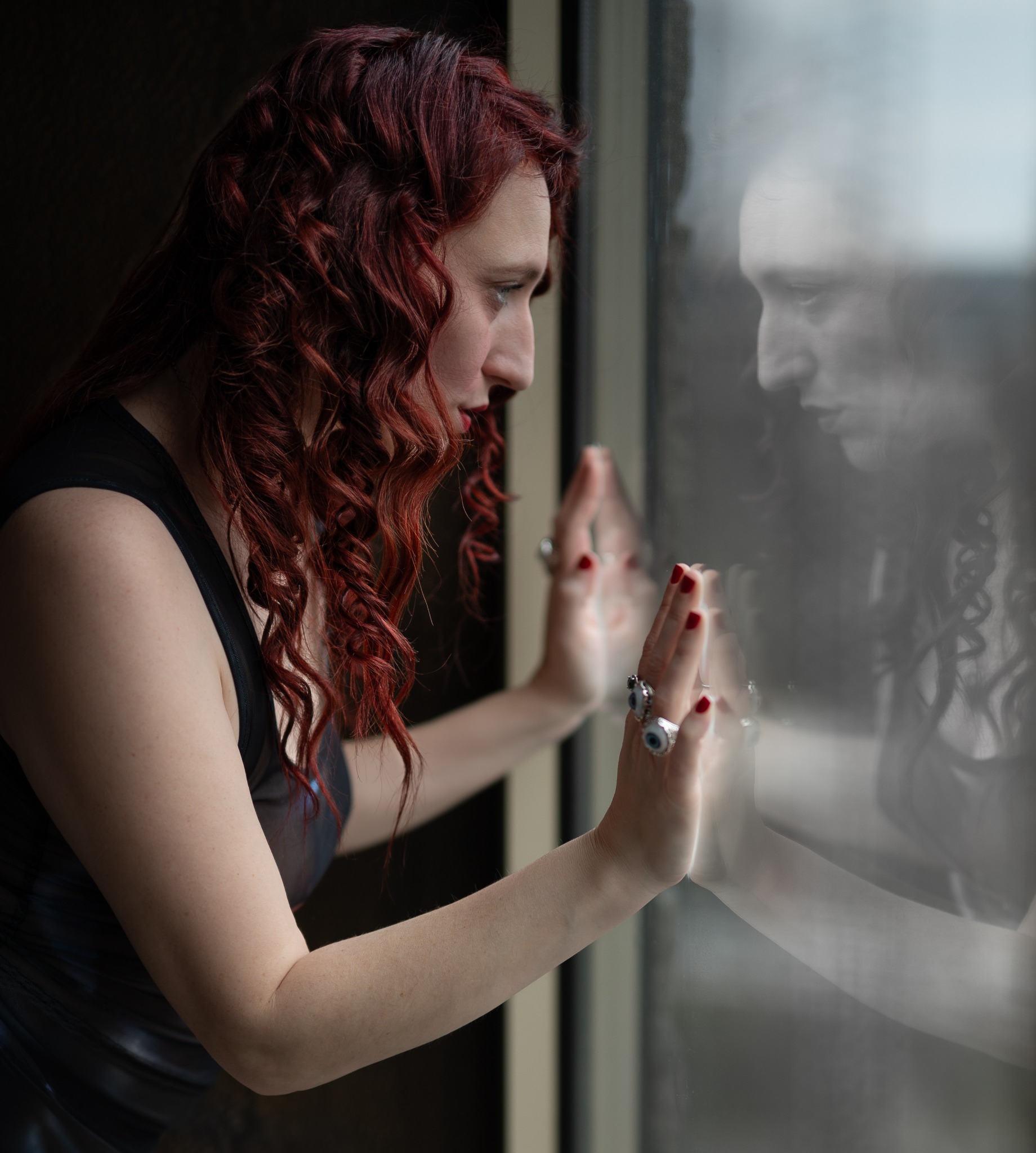 Reflective portrait of a red-haired woman touching a window