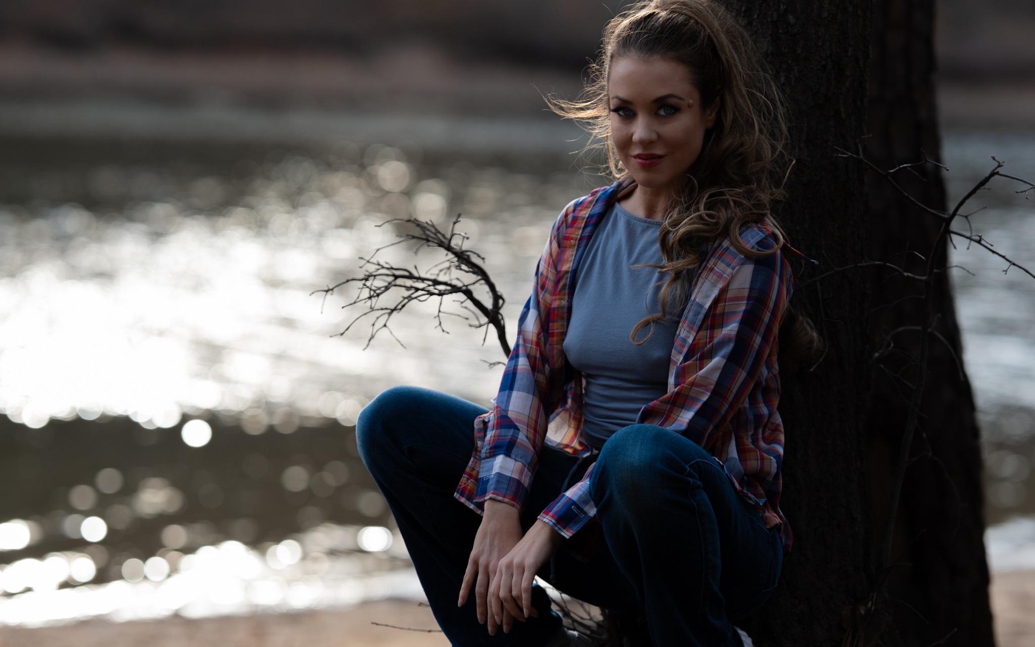 Lakeside portrait of a woman in plaid seated beside a tree